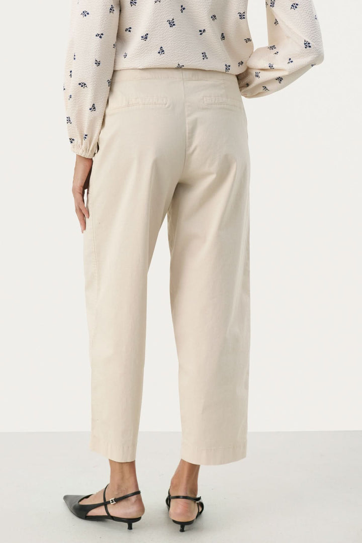 Pantalon Netta beige à coupe décontractée, avec grandes poches et tissu en coton extensible, porté avec blouse fluide.