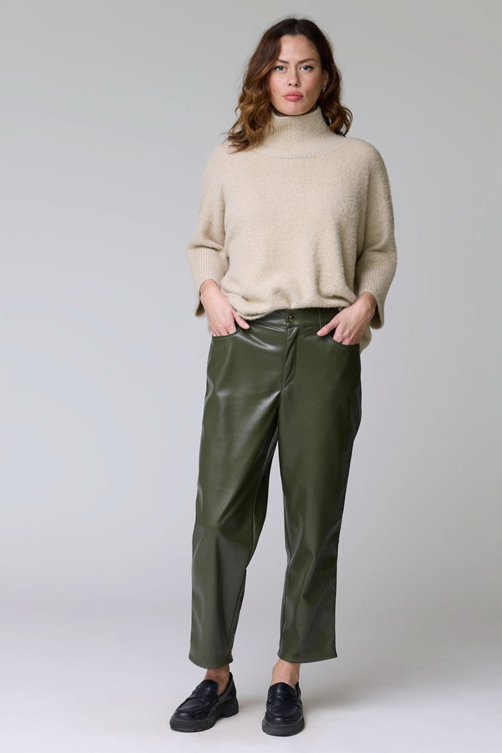 Femme portant un Pantalon Sabrna effet cuir avec un pull beige, coupe droite, style urbain et contemporain. Décrit le produit en français.