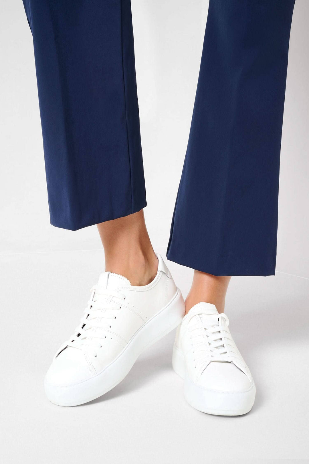 Femme portant des pantalons bootcut Shakira et des baskets blanches sur fond neutre.