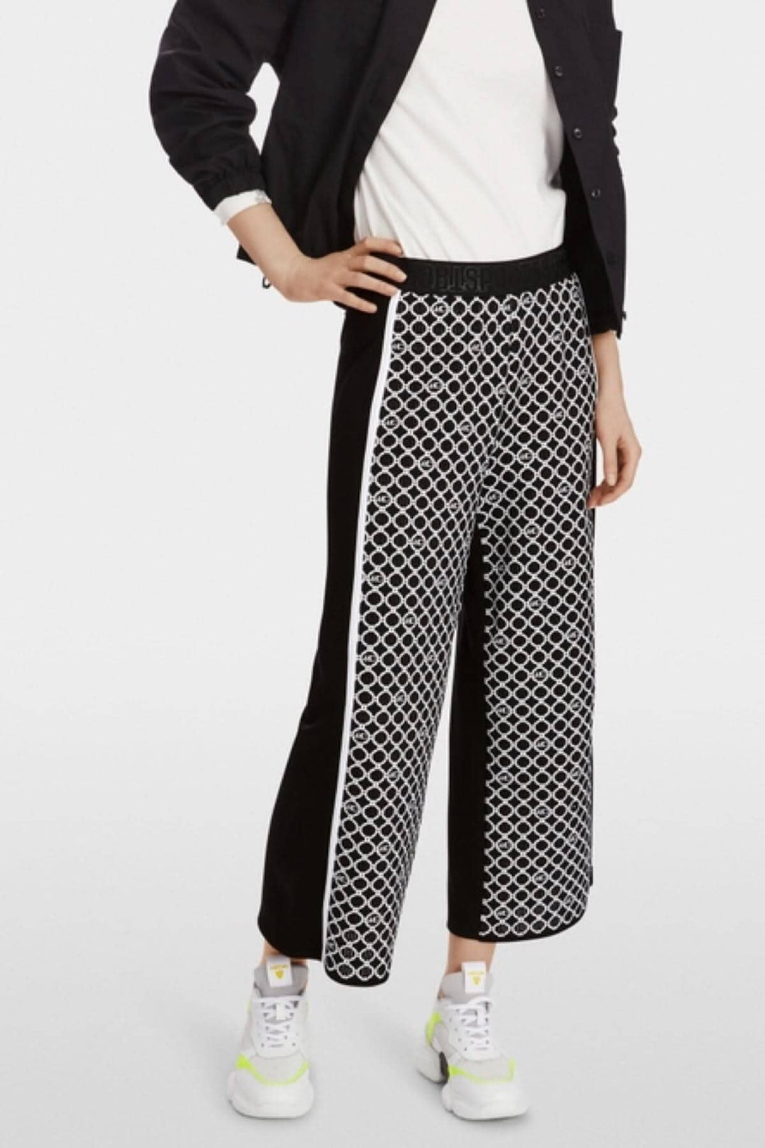 Pantalon WUSU noir et blanc à motif de chaînes, avec ceinture élastique, porté avec des baskets blanches.