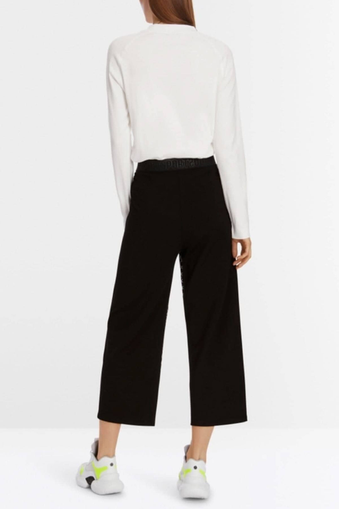 Pantalon WUSU large en mélange de matières, avec ceinture élastique, porté avec un pull blanc et des chaussures colorées.