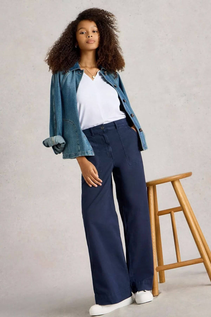 Femme portant un pantalon ample à taille haute avec une chemise en denim et un t-shirt blanc, devant un tabouret en bois.