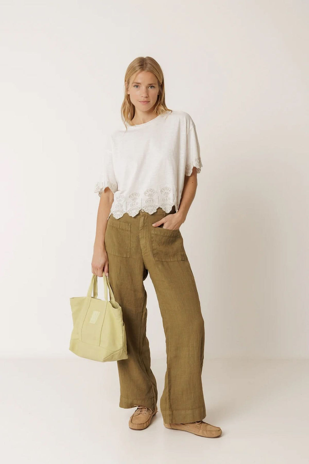 Femme portant un pantalon ample en lin à poches plaquées avec un t-shirt blanc, décontracté et élégant, et sac jaune vif.