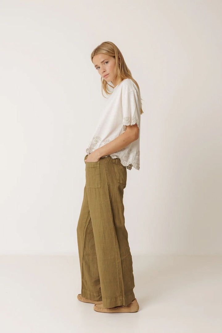 Femme portant un pantalon ample en lin à poches plaquées, décontracté et moderne, avec un t-shirt blanc de style fluide.