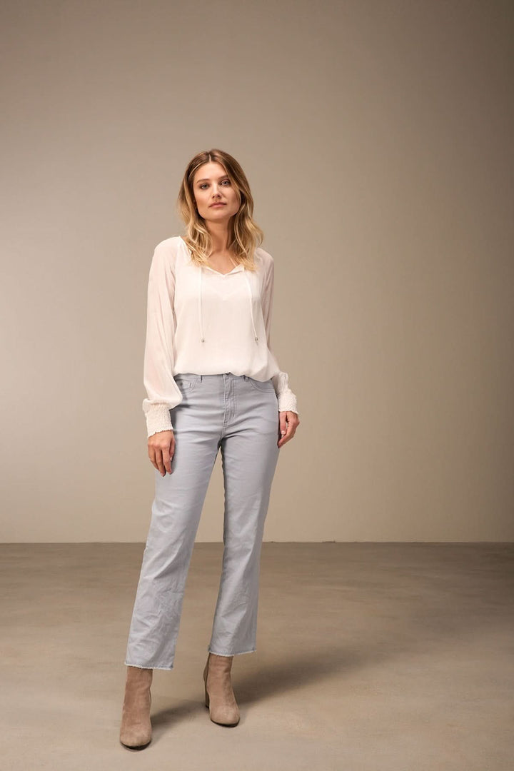 Femme portant un pantalon bootcut chic et une blouse fluide, stylée avec des bottines, dans un cadre sobre.