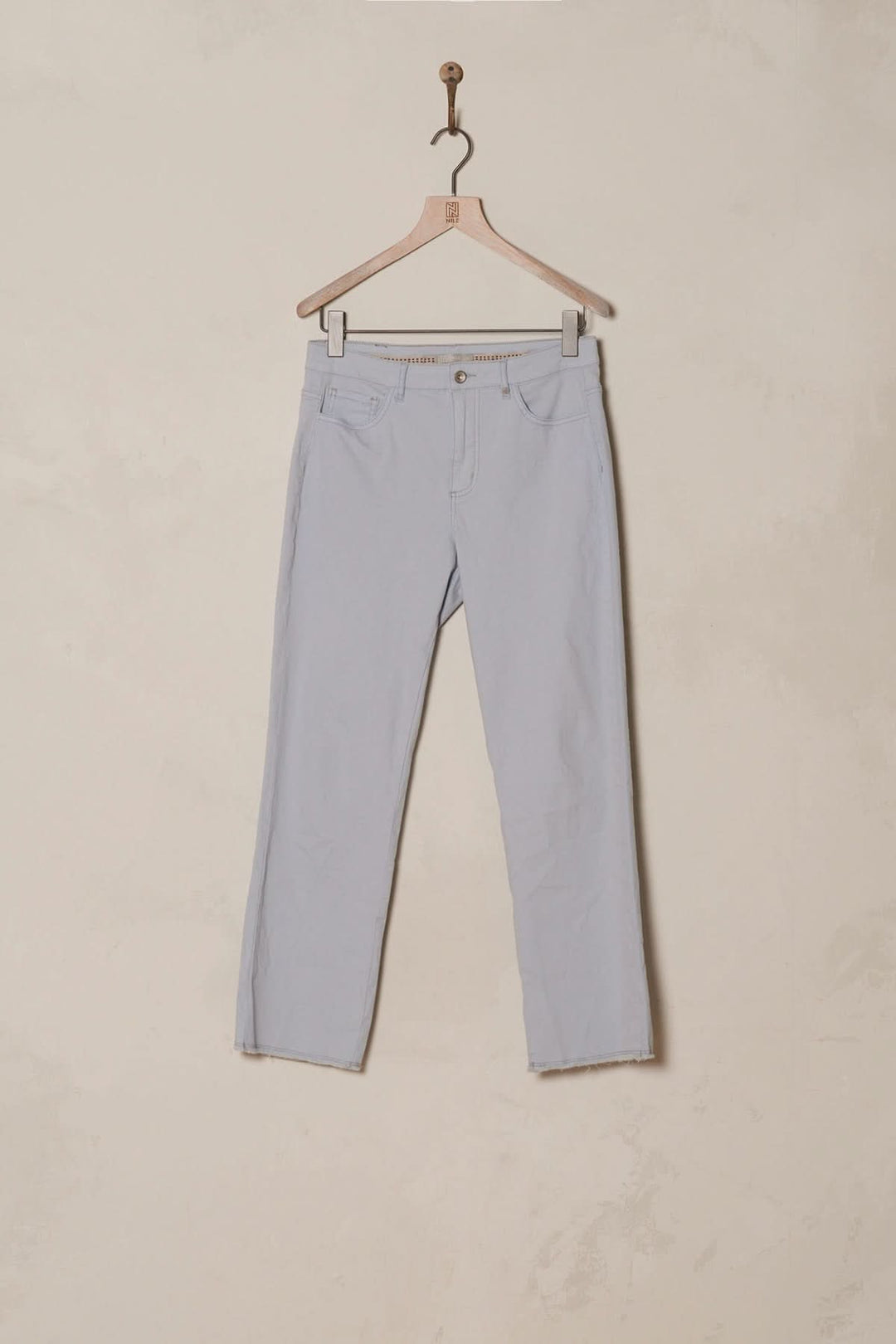 Pantalon bootcut bleu clair avec bordure à franges, style bohème et coupe évasée, suspendu sur un cintre.