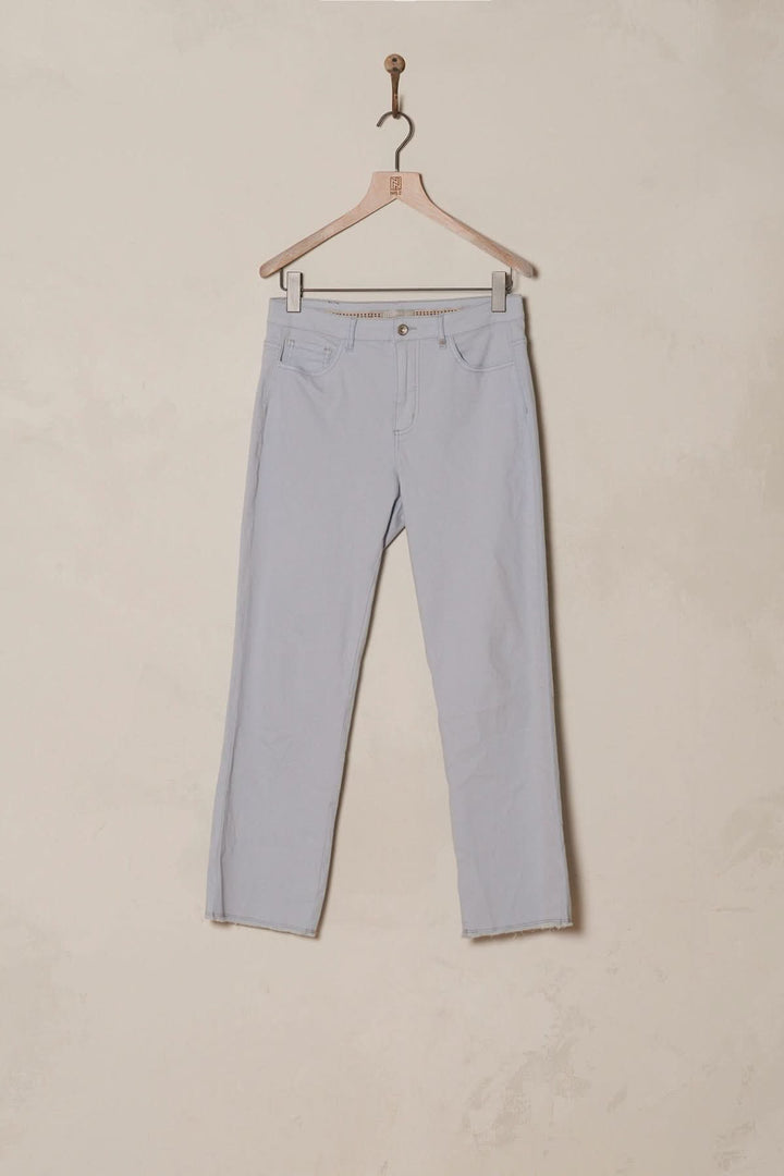 Pantalon bootcut bleu clair avec bordure à franges, style bohème et coupe évasée, suspendu sur un cintre.