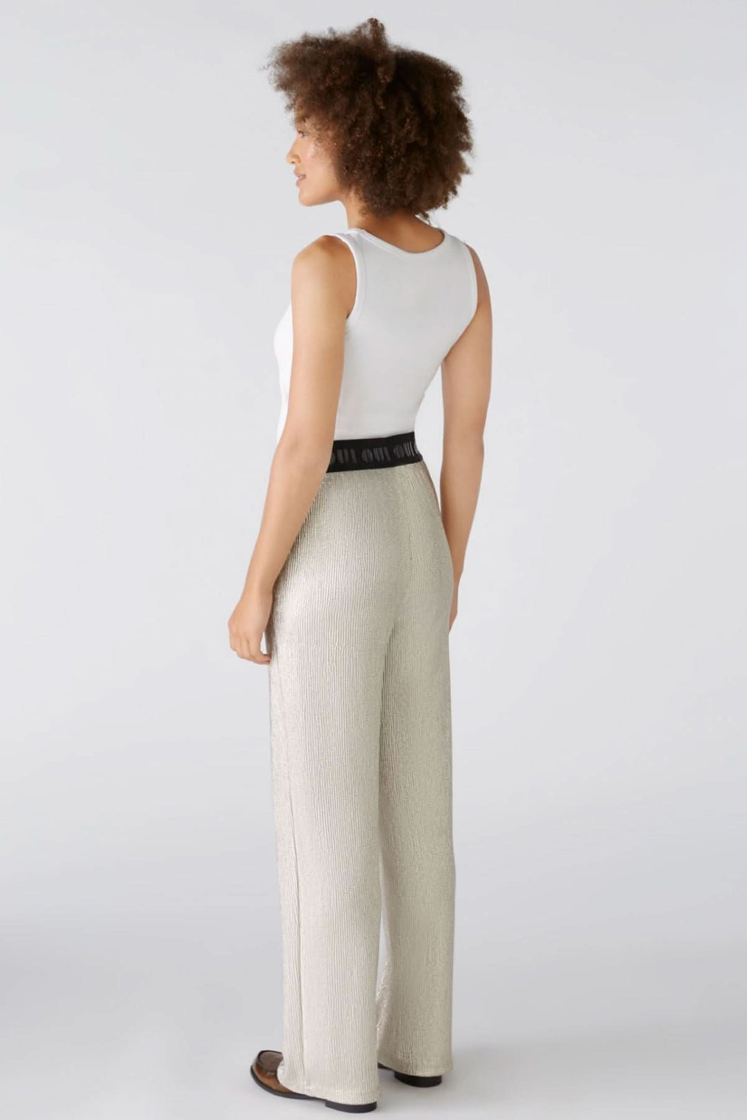 Femme portant un pantalon brillant extensible avec une ceinture élastique, vu de dos.