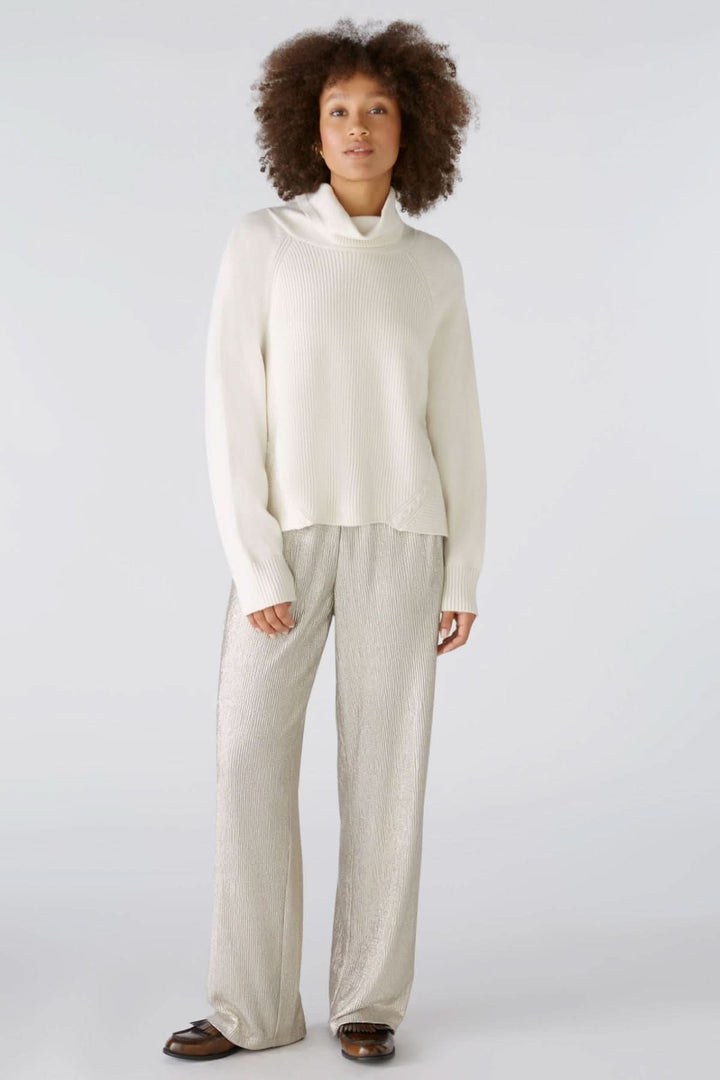 Femme portant un pullover blanc et pantalon brillant, idéal pour une tenue décontractée ou festive.