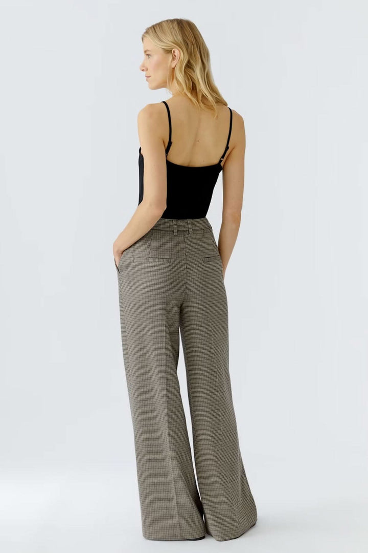 Femme portant un pantalon à carreaux ample et fluide, taille régulière avec plis français, offrant un look professionnel.