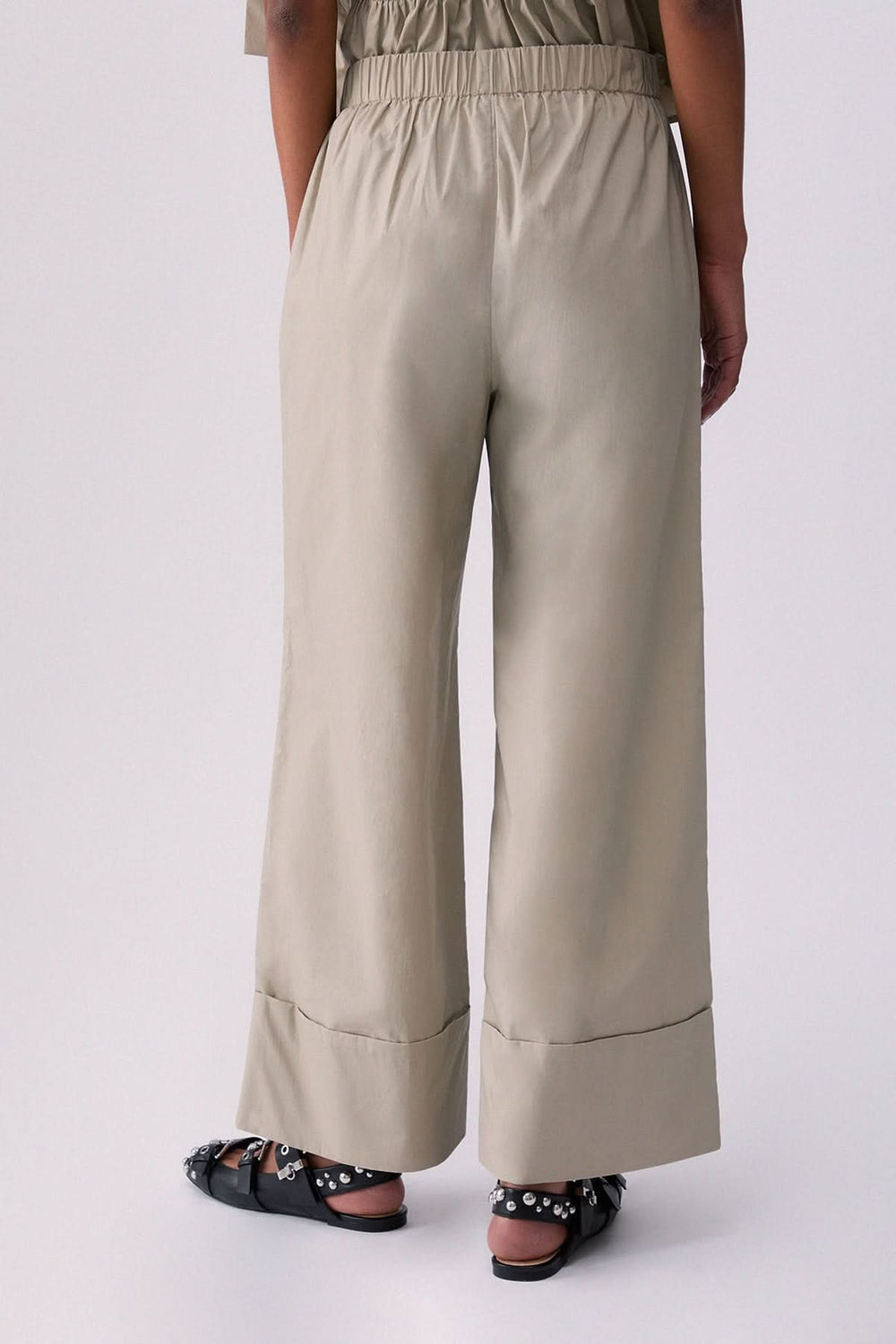 Pantalon chino à jambe large beige avec revers et poches latérales, porté par une personne de dos, décris moi le produit en français.