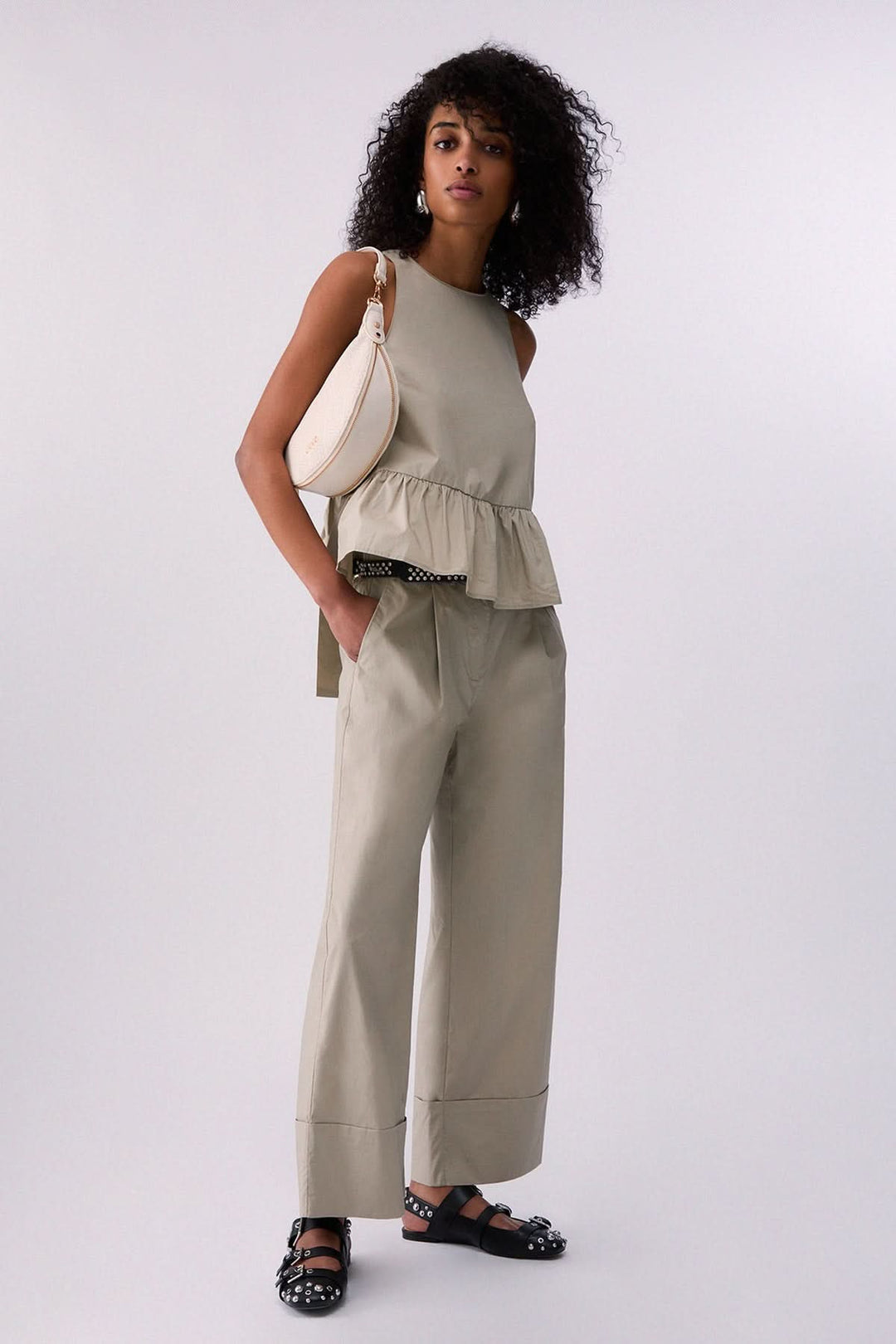 Femme portant un pantalon chino à jambe large avec un haut sans manches, sac à main blanc et sandales décorées, décris moi le produit en français.