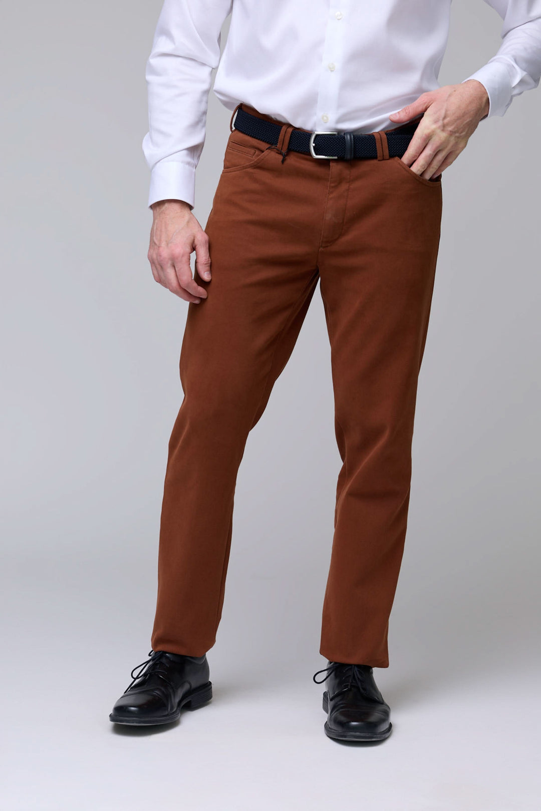 Homme portant un pantalon chino moderne marron avec chemise blanche, coupe droite élégante, tissu extensible pour confort optimal.