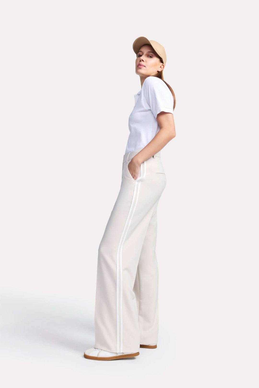 Pantalon classique Amelie à jambe large avec bandes contrastantes, associé à un polo blanc et une casquette beige.