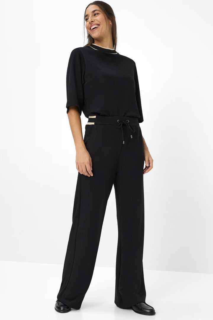 Femme portant un pantalon noir à coupe ample avec taille élastiquée et ceinture à cordon ajustable.