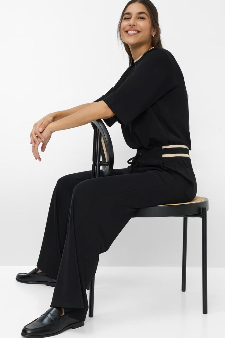 Pantalon coupe Maine noir avec taille élastiquée, ceinture à cordon et détail moderne, porté sur une chaise.
