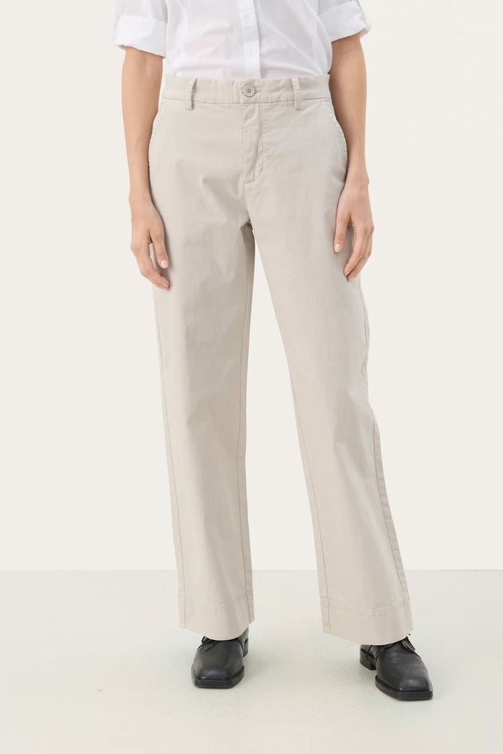 Personne portant un pantalon à coupe droite beige en coton et élasthanne, avec une chemise blanche, alliant confort et élégance.