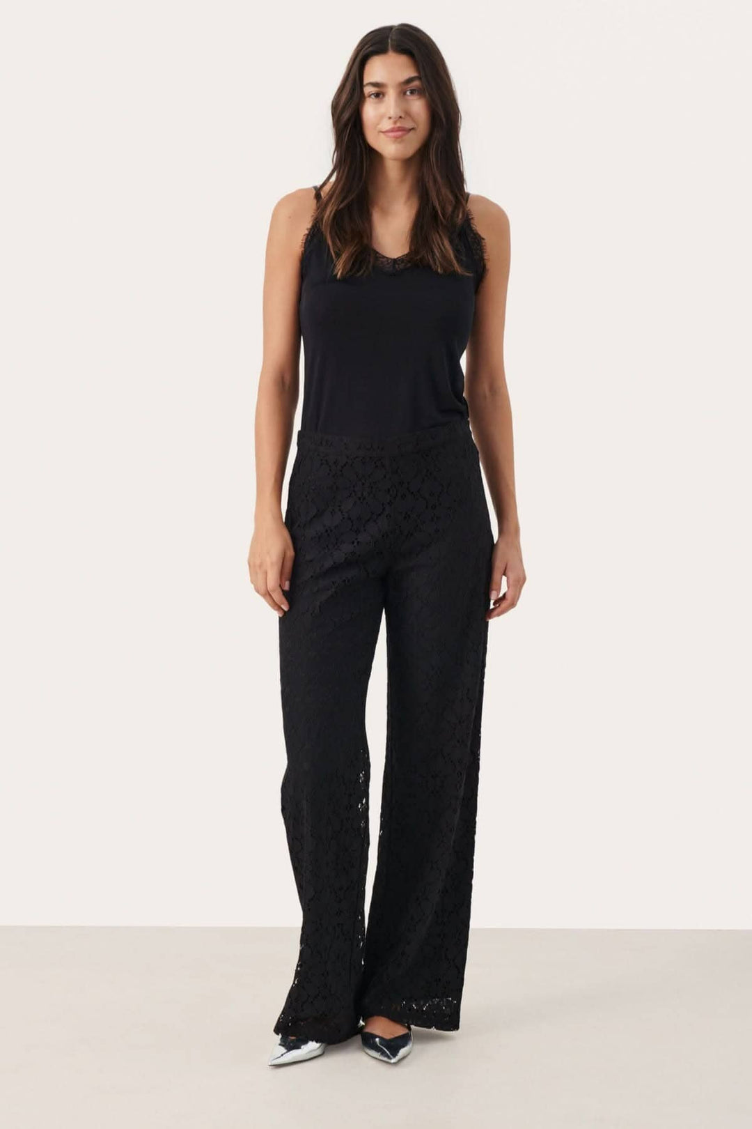 Pantalon de dentelle noir Devi, coupe classique, jambe droite et taille dissimulée, portée avec un haut noir.