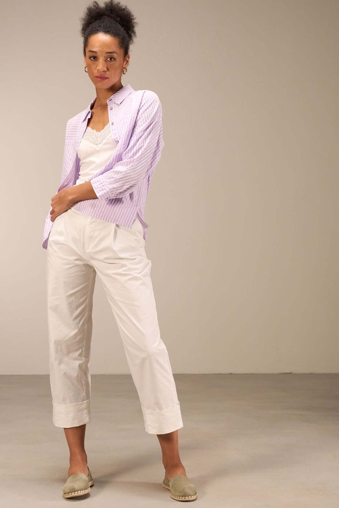 Modèle féminin portant un pantalon droit blanc et chemise rayée violette, mettant en avant confort et élégance estivale.
