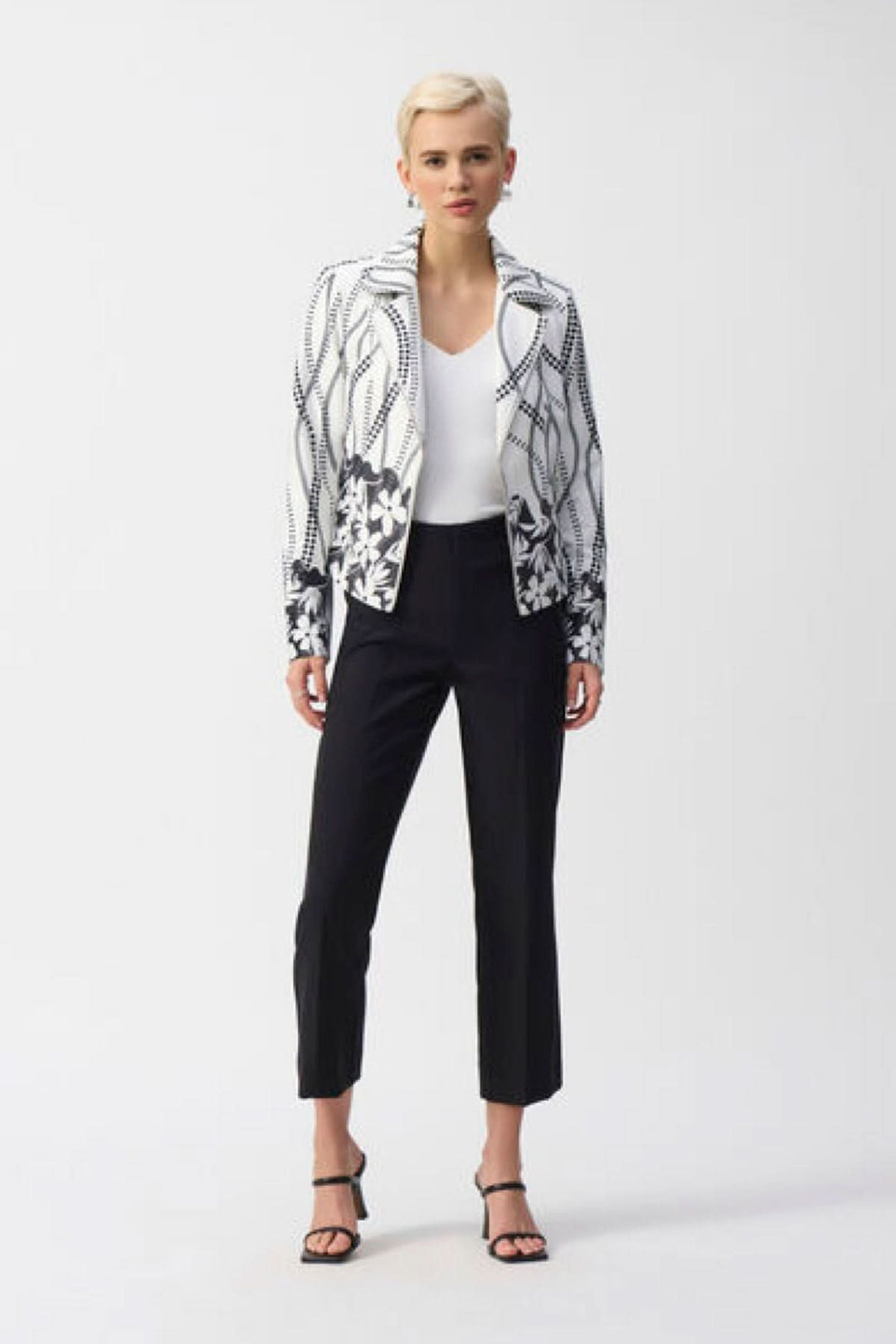 Femme portant un pantalon droit noir, veste à motifs, et sandales, émettant une allure chic et décontractée.