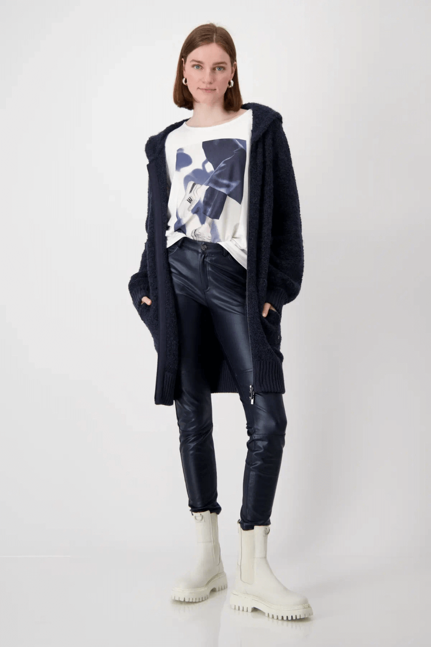 Femme portant un pantalon effet cuir noir avec un haut graphique et un cardigan long, chaussures blanches.