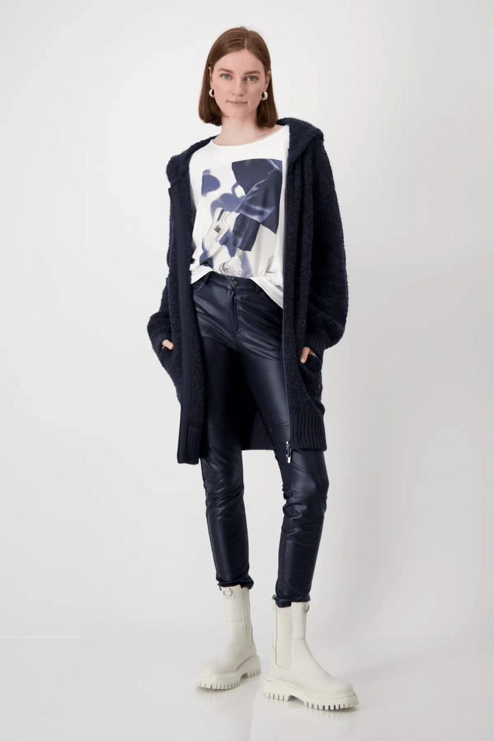 Femme portant un pantalon effet cuir noir avec un haut graphique et un cardigan long, chaussures blanches.