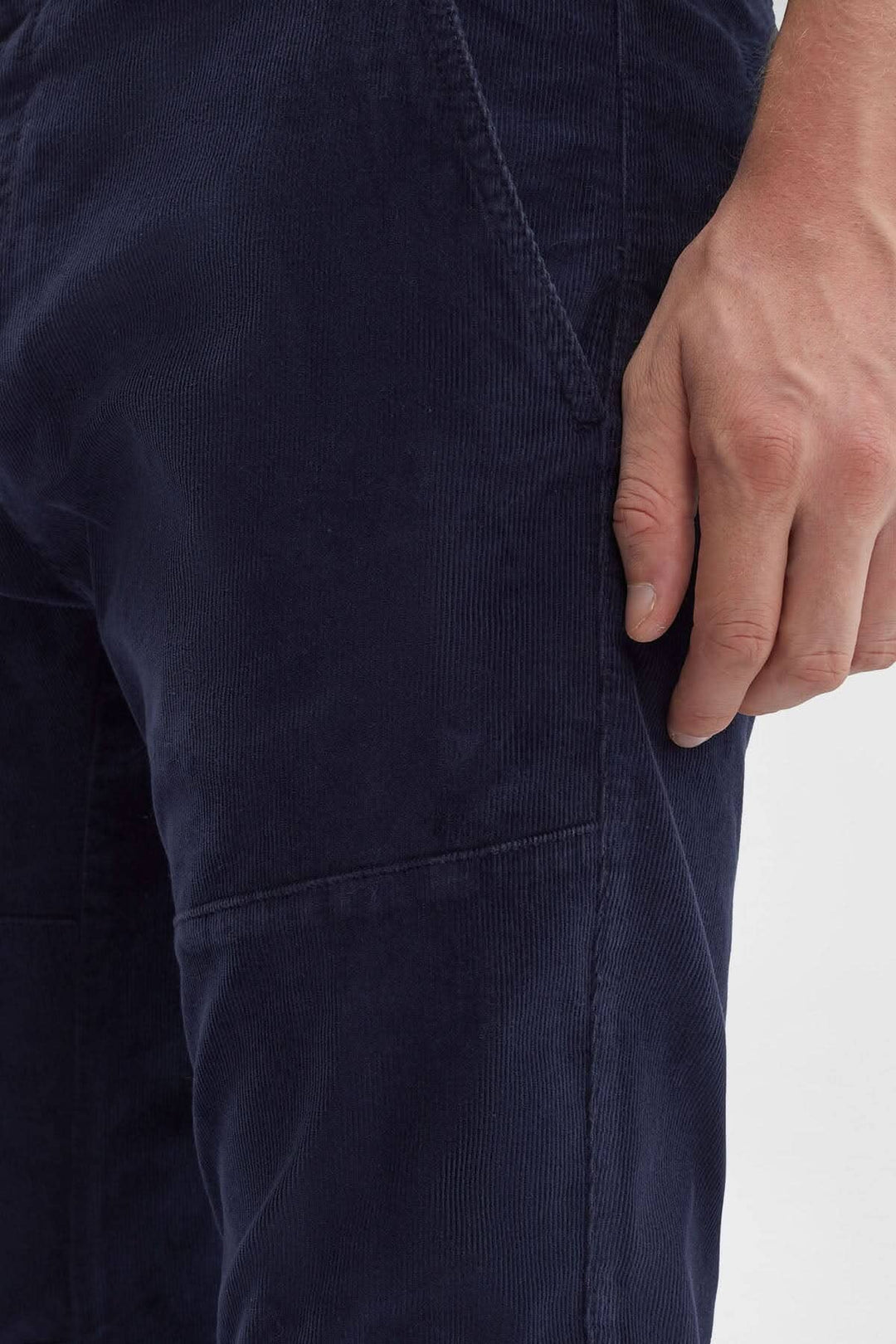 Détail du pantalon en velours côtelé, montrant la texture et la coupe ergonomique, avec une main dessus.