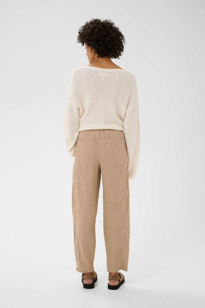Dos d'une femme portant un Pantalon en lin Atima beige avec une coupe droite et un pull crème, stylé et confortable.