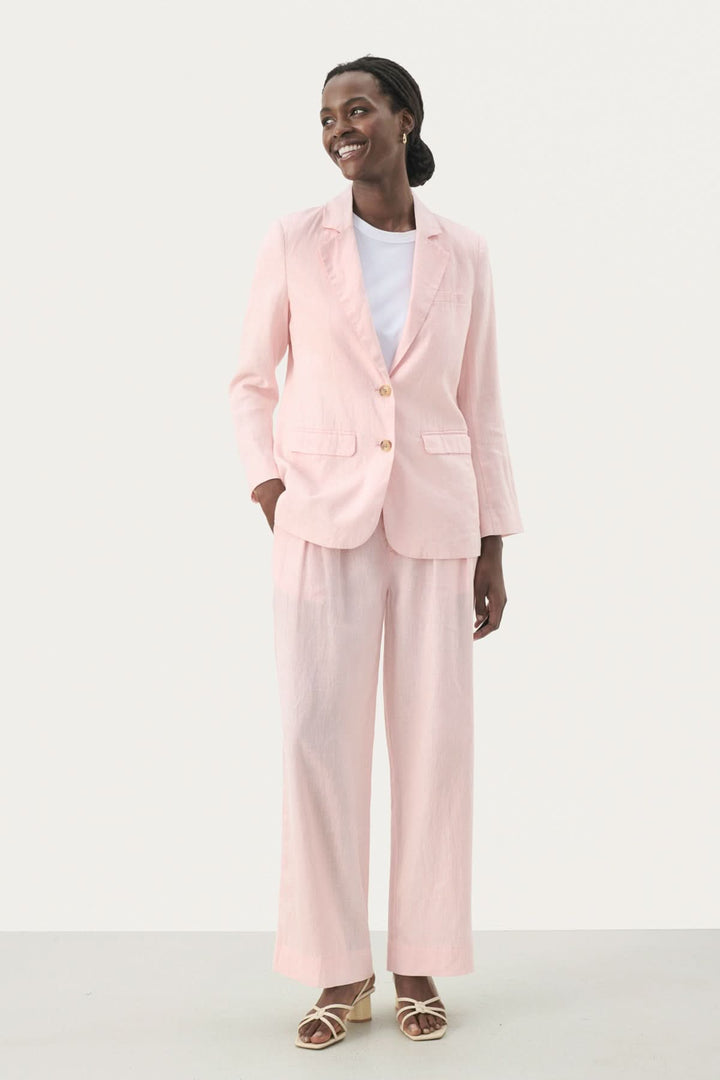 Femme souriante portant un ensemble tailleur en lin rose, composé d'une veste et pantalon à jambes larges.