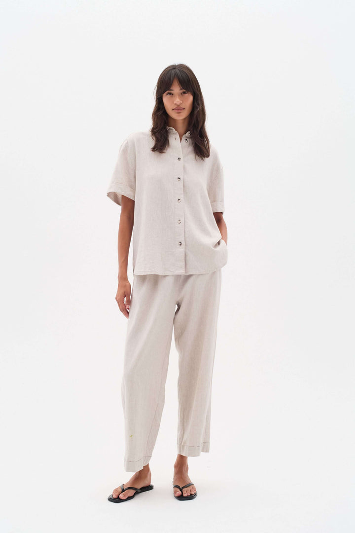 Femme portant un ensemble en lin avec chemise à boutons et pantalon large, style confortable et élégant.