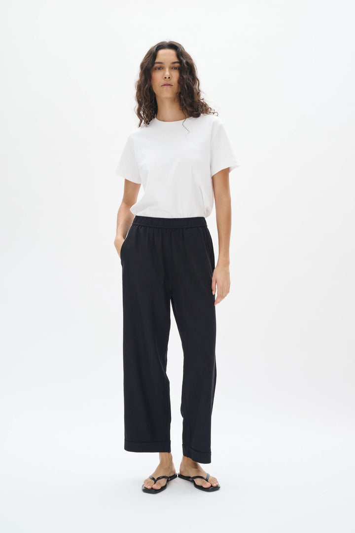 Femme portant un pantalon en lin noir avec taille élastique et t-shirt blanc, affichant un style décontracté.