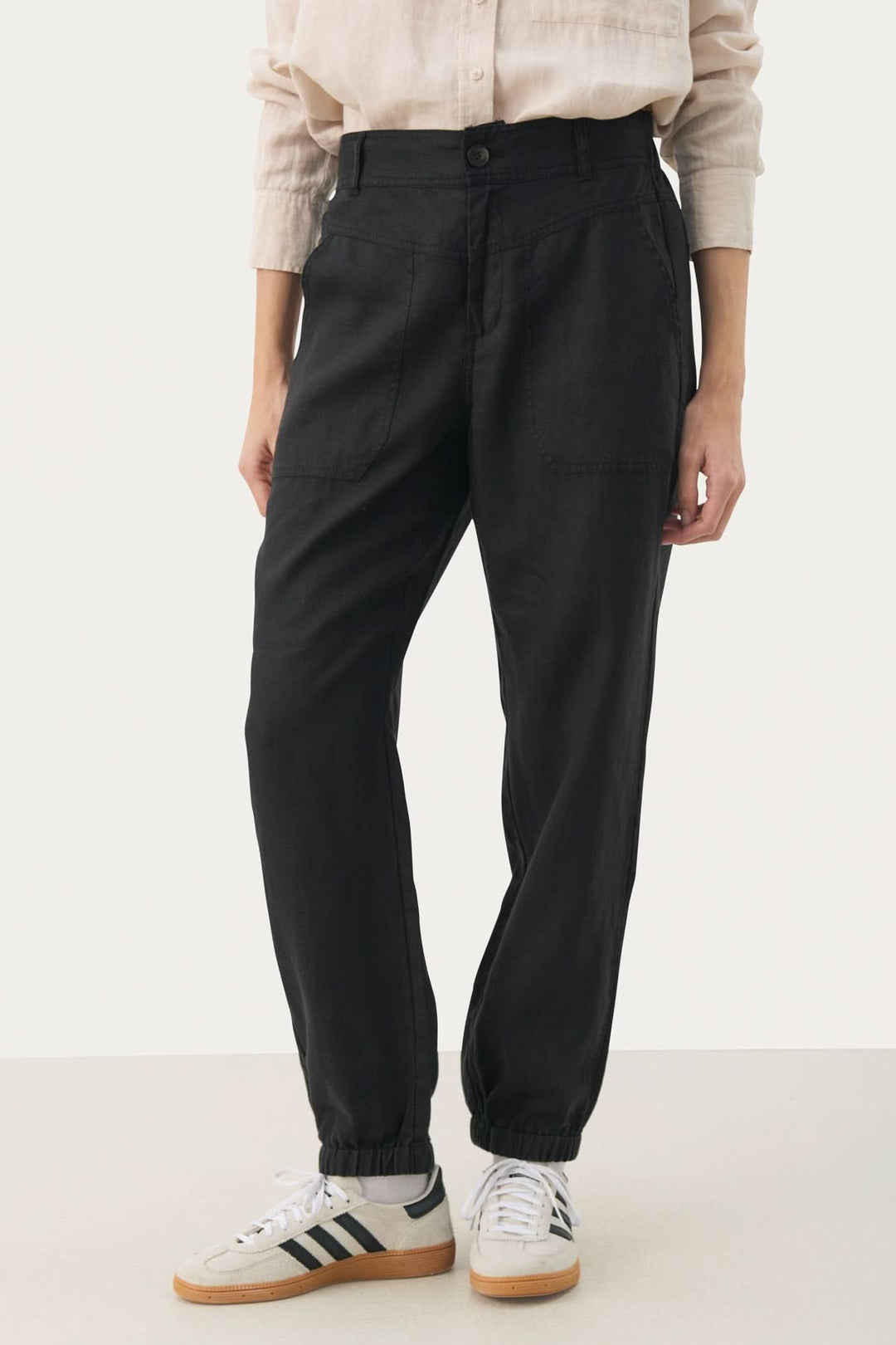 Pantalon en lin Shenas noir, coupe ample avec poches avant et chevilles élastiques, porté avec des sneakers.