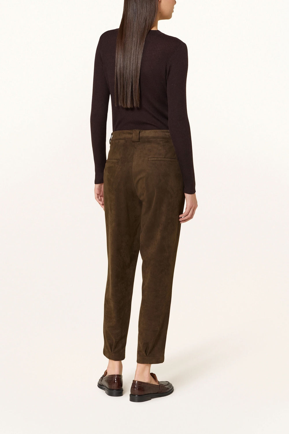 Femme portant un pantalon en suédine à pinces, chic et décontracté, avec taille mi-haute et coupe légèrement fuselée, vu de dos.