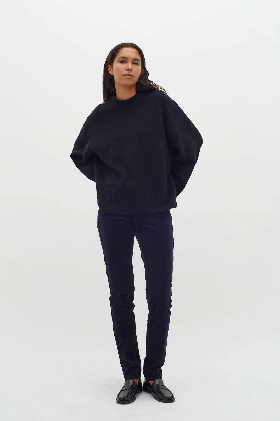 Femme portant un pantalon en velours bleu marine avec un pull noir, arrière-plan blanc.