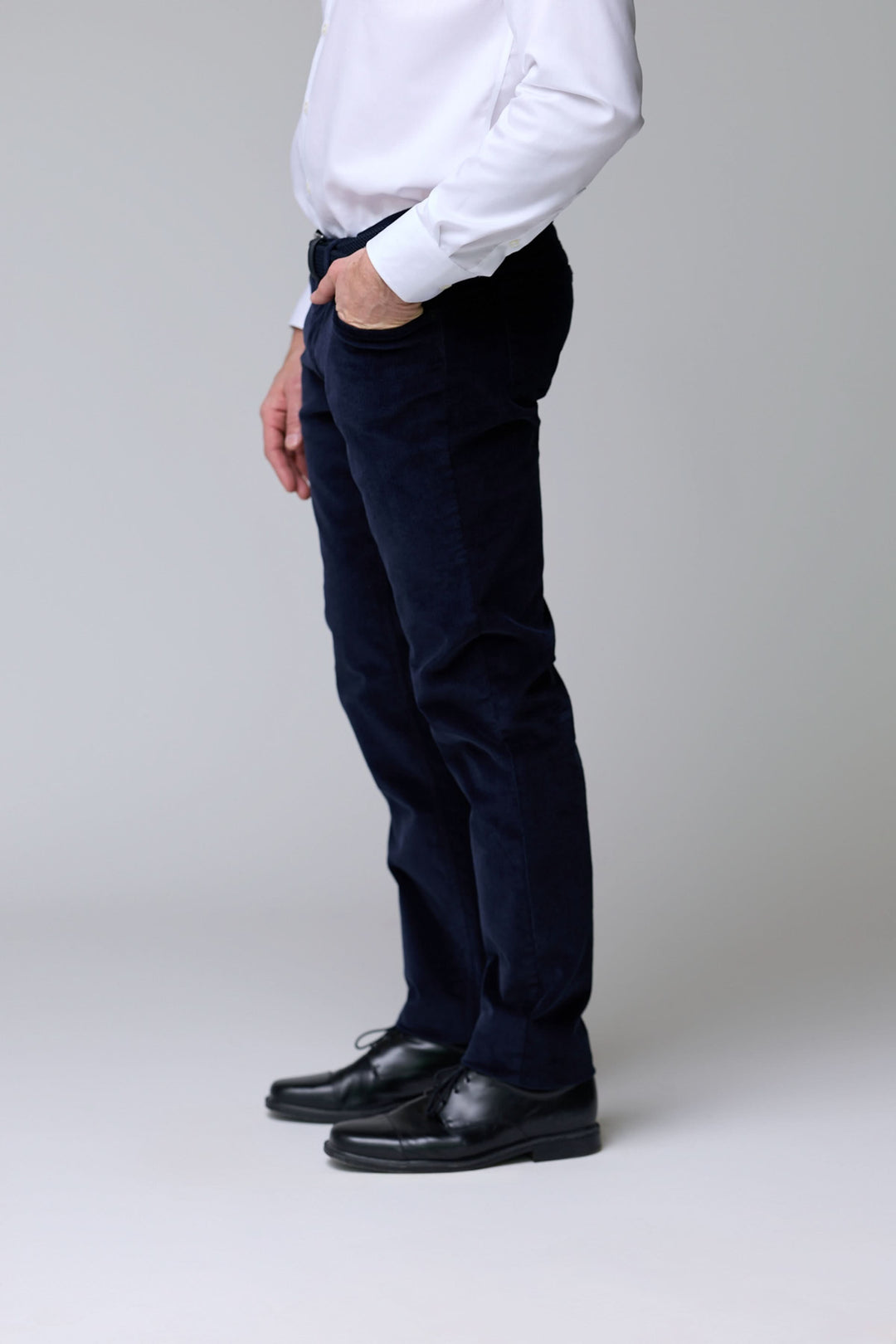 Homme portant un pantalon en velours côtelé bleu marine avec chemise blanche et chaussures noires, vue latérale, style élégant.
