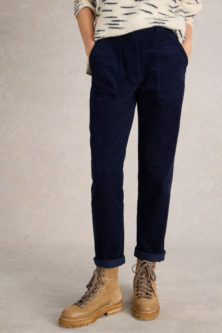 Pantalon en velours côtelé bleu marine, coupe droite, porté avec des bottes, sur fond neutre.
