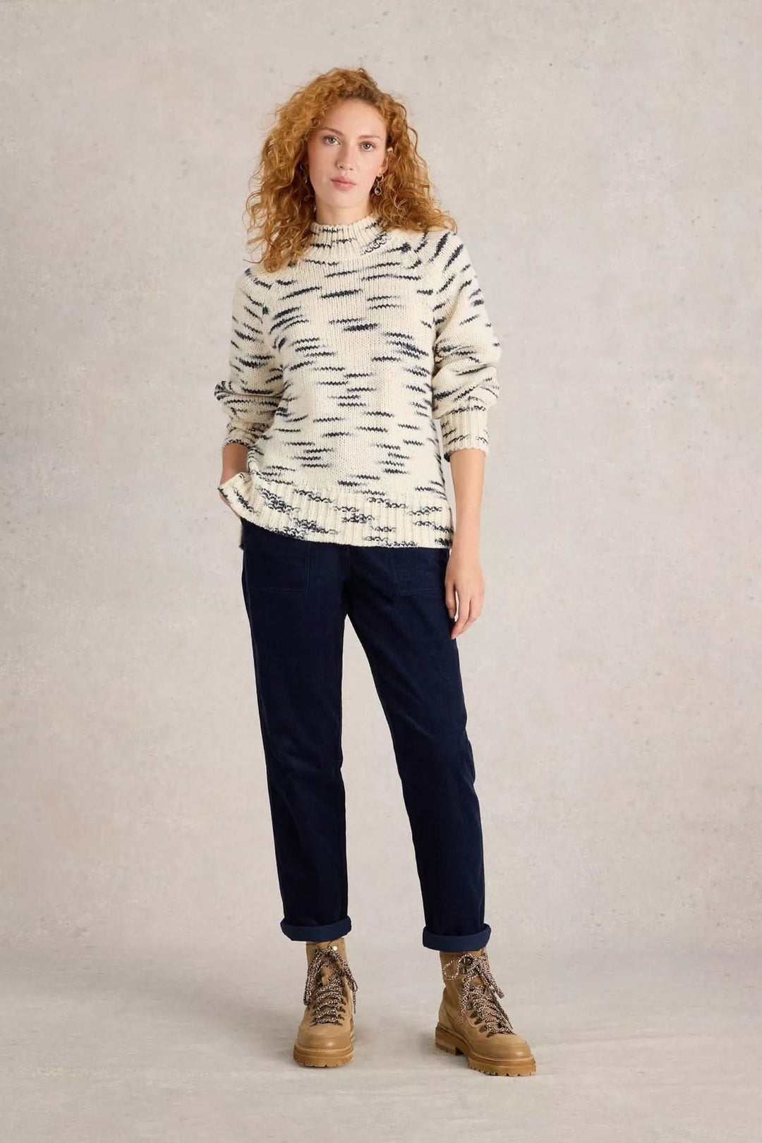 Femme portant un pull en maille beige et un pantalon en velours côtelé noir, avec des bottes marron.