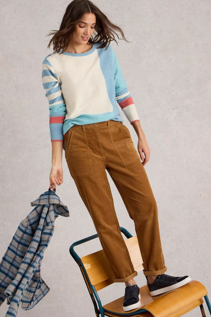 Femme portant un pantalon en velours côtelé couleur marron avec un pull style décontracté, assise sur une chaise en bois.