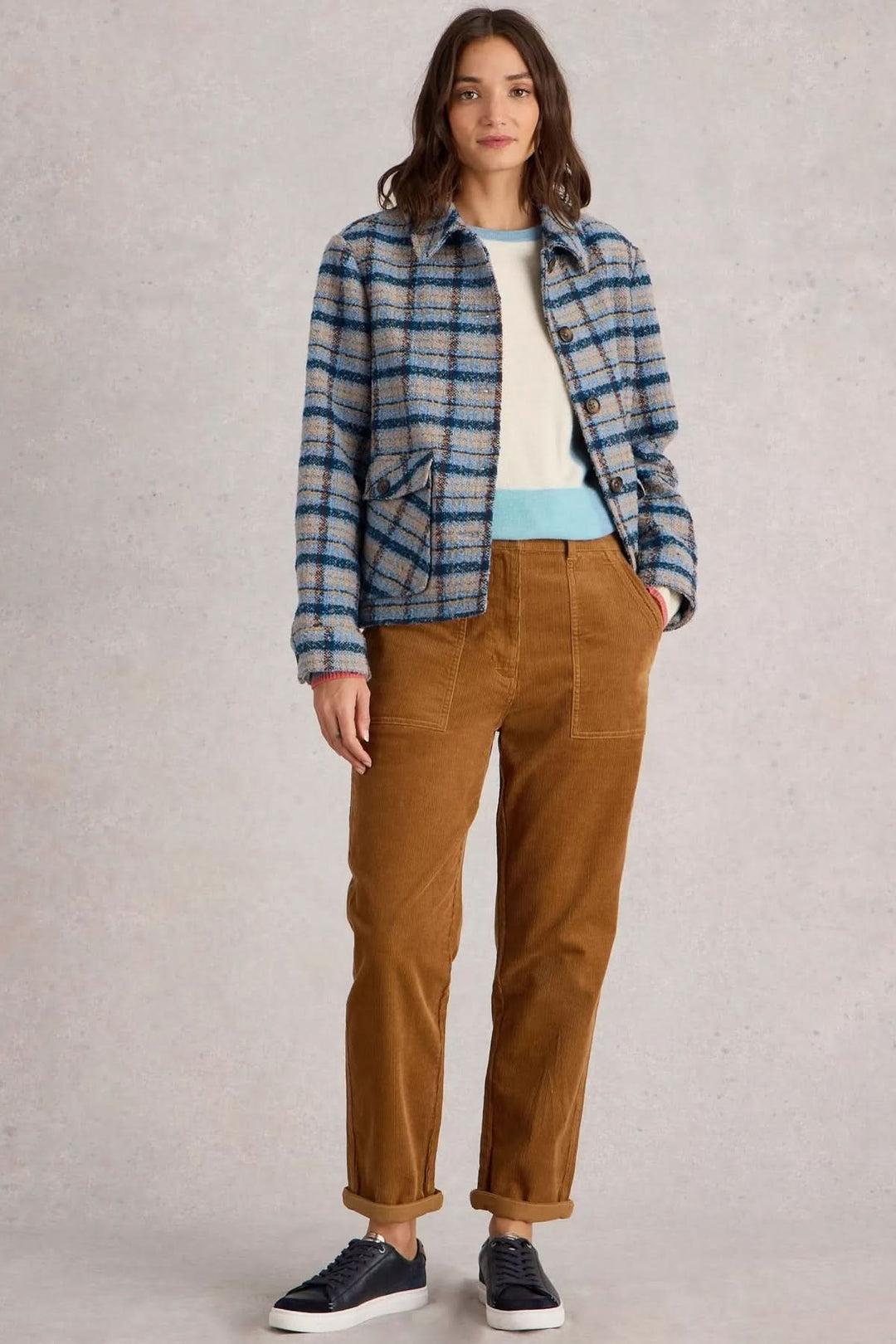 Femme portant un pantalon en velours côtelé marron et une veste à carreaux bleus, style décontracté.