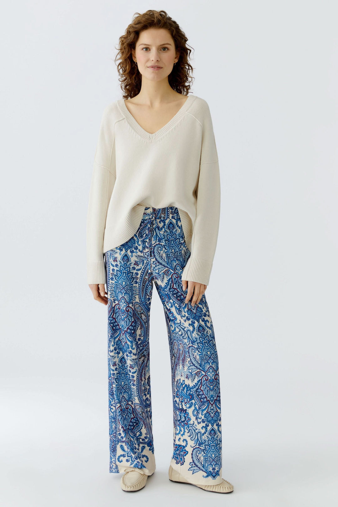 Pantalon fluide à imprimé cachemire bohème porté par une femme, style élégant avec chandail en maille pour un look raffiné et confortable.