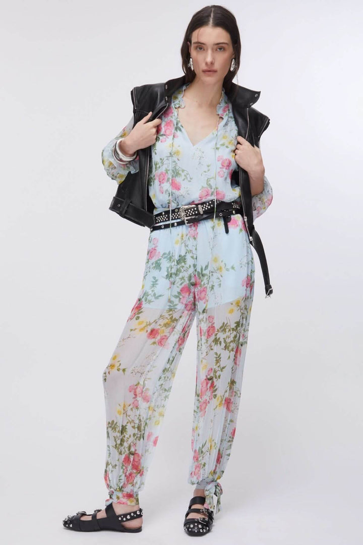 Femme portant un pantalon fluide à imprimé floral avec blouse assortie et veste noire, style estival élégant.