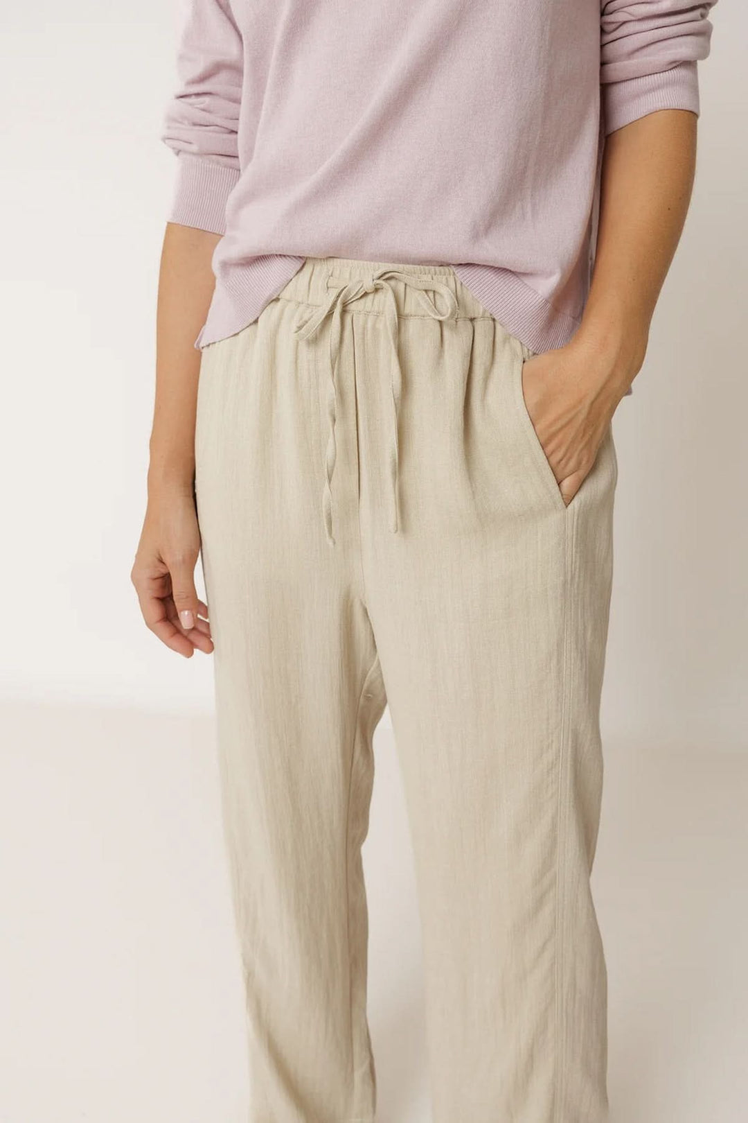 Pantalon fluide à taille élastique avec cordon, coupe droite ample, couleur neutre, porté avec un haut lilas pour un style décontracté.