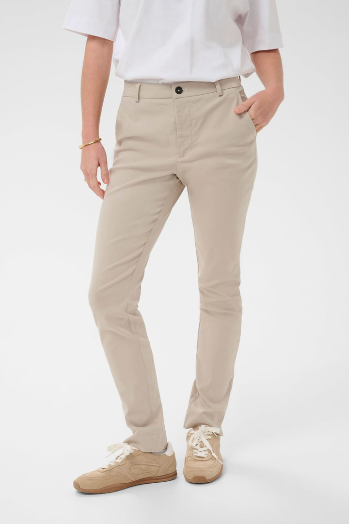 Homme portant un Pantalon habillé Hazel beige avec chemise blanche et baskets, coupe ajustée élégante pour un look professionnel.