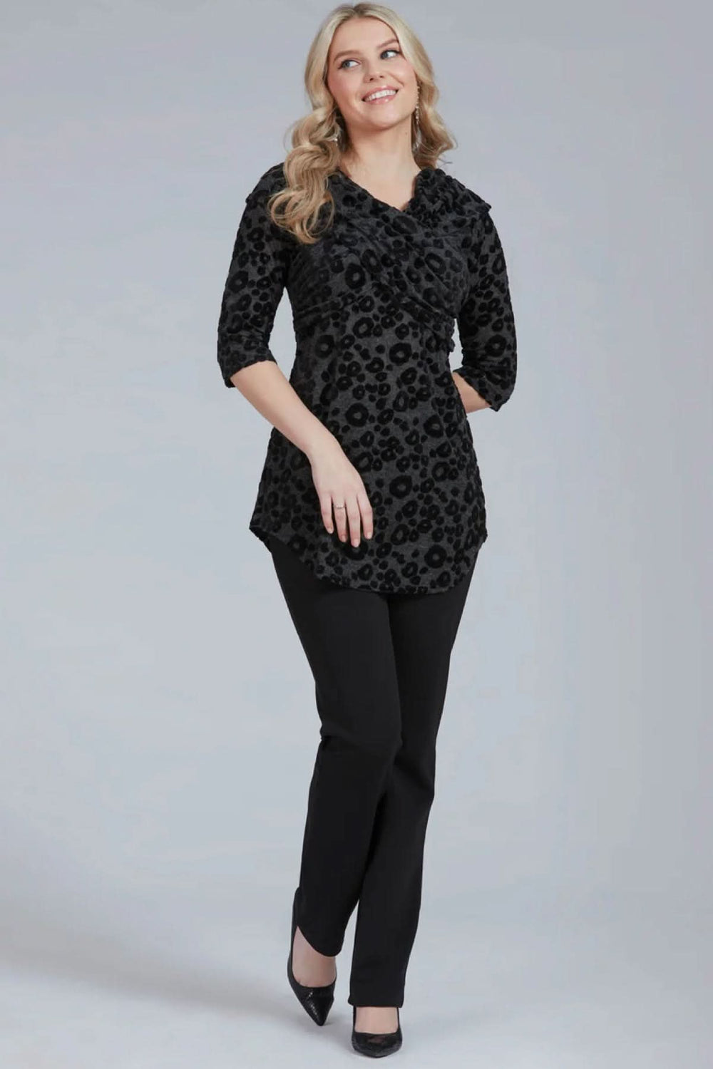 Modèle portant un pantalon habillé Tucker avec blouse noire à motifs, look chic et élégant.