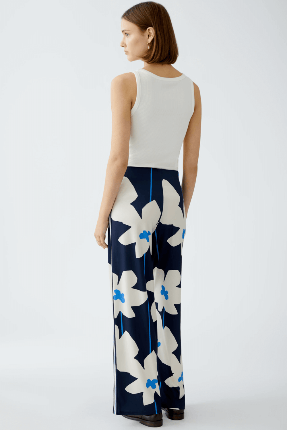 Femme de dos portant un pantalon imprimé floral navy, style ample et élégant, associé à un haut uni blanc.