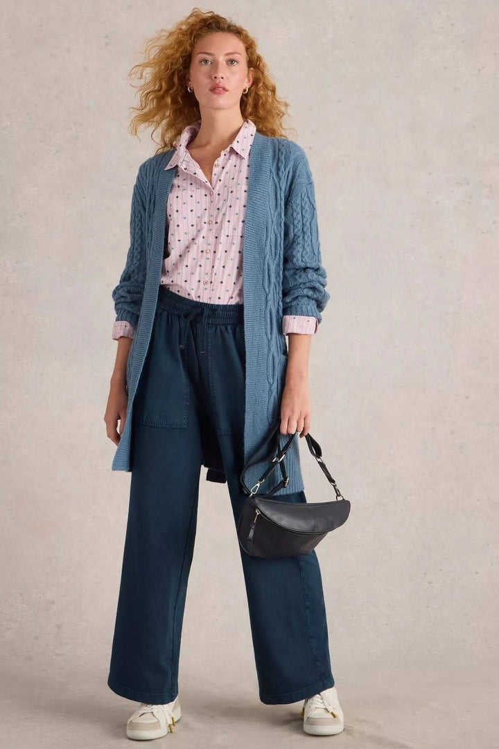 Femme en pantalon à jambe large et gilet bleu, tenue décontractée avec chaussures blanches et sac noir.