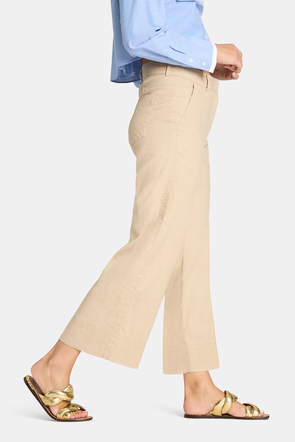 Pantalon à jambe large Cara en beige, porté avec une chemise bleue et des sandales dorées, offrant un style moderne et épuré.