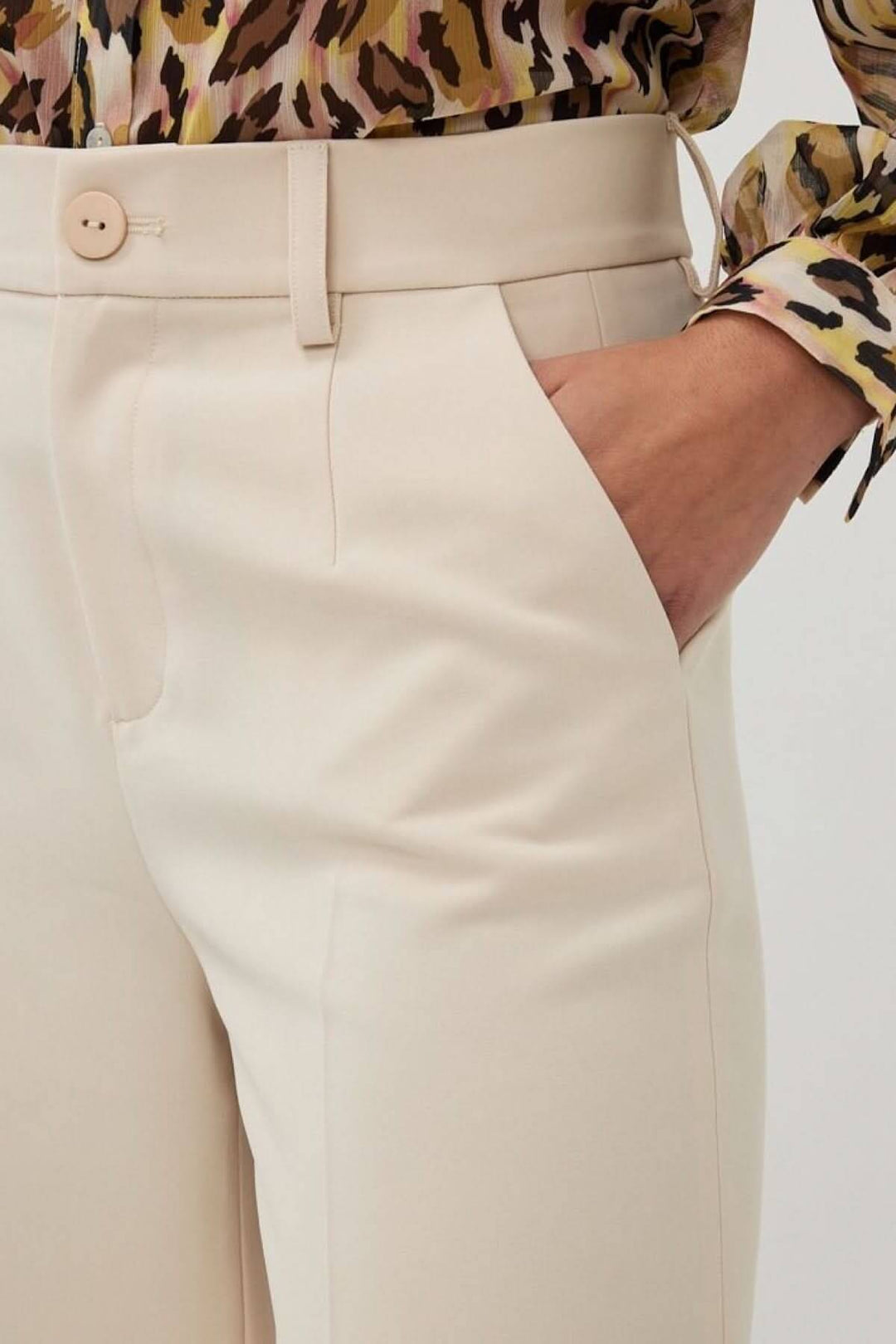 Pantalon à jambe large beige avec taille haute et poches, porté avec un chemisier à motifs colorés.