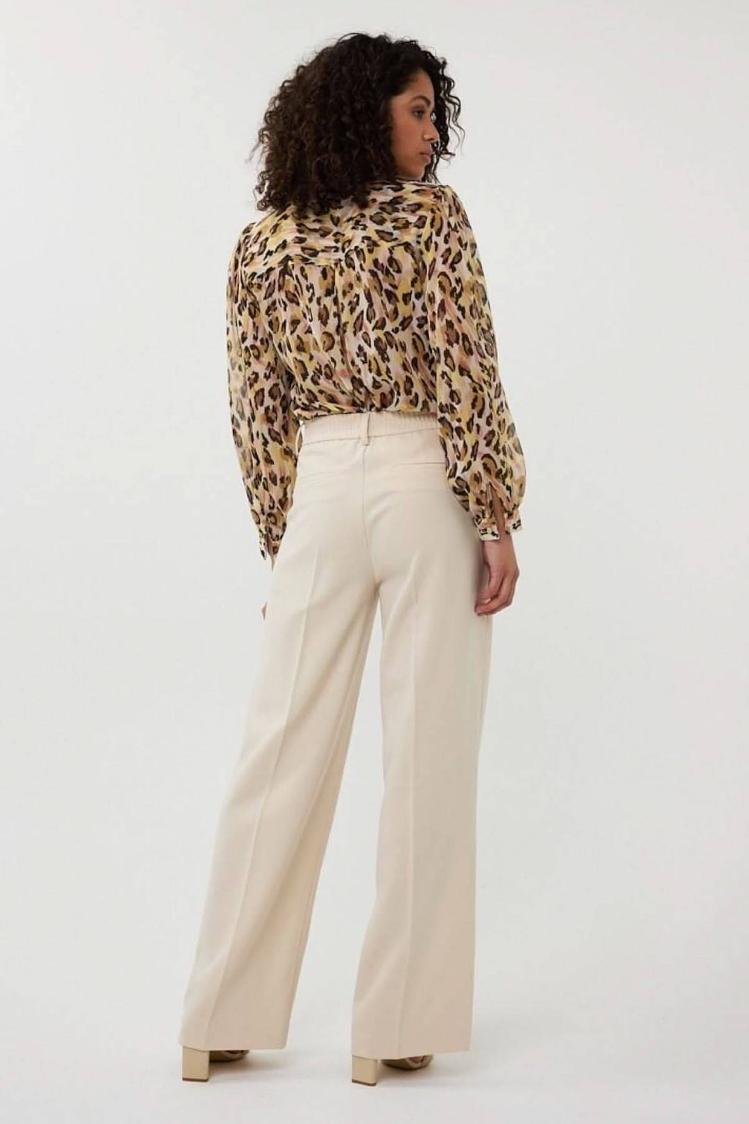 Femme portant un pantalon à jambe large beige avec un chemisier à motifs léopard, vue de dos.