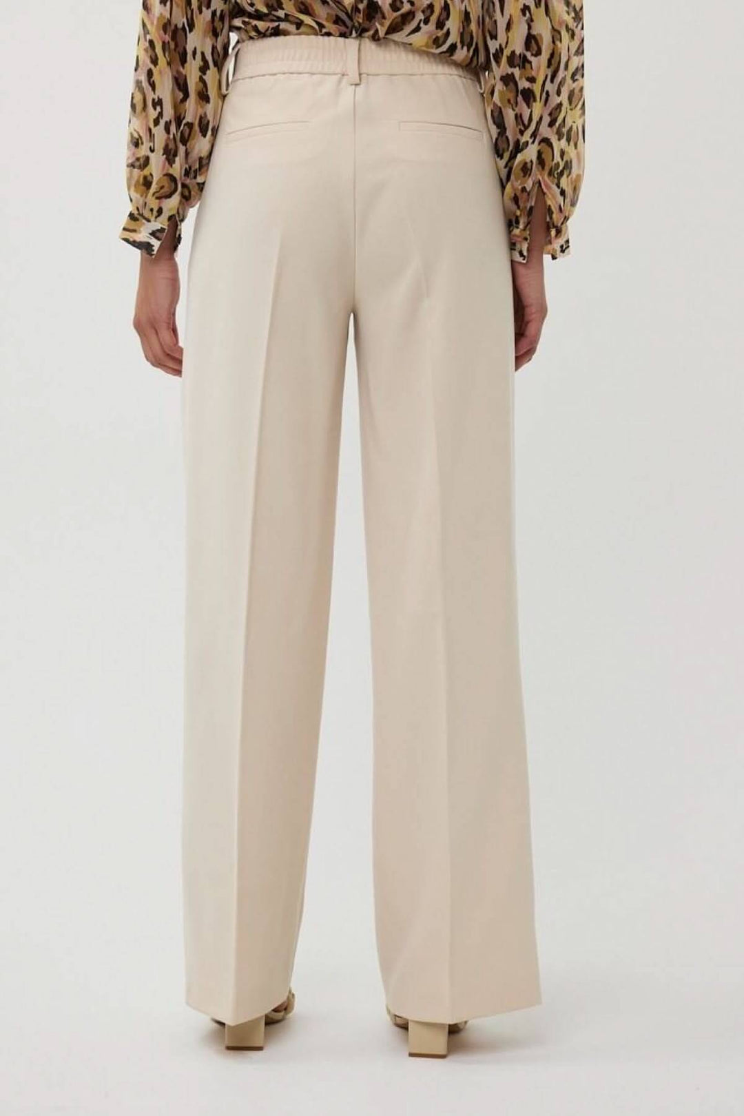 Pantalon à jambe large beige avec taille haute et plis, porté vue arrière, idéal pour un look professionnel.